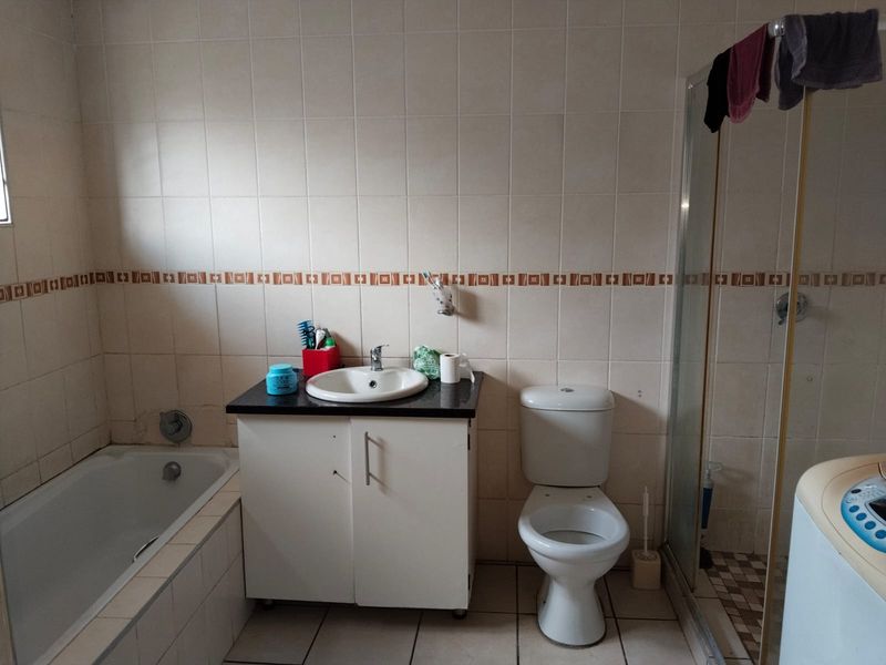 A functional bathroom featuring a built-in vanity, bathtub, separate shower enclosure, and toilet, with full-height wall tiling throughout.