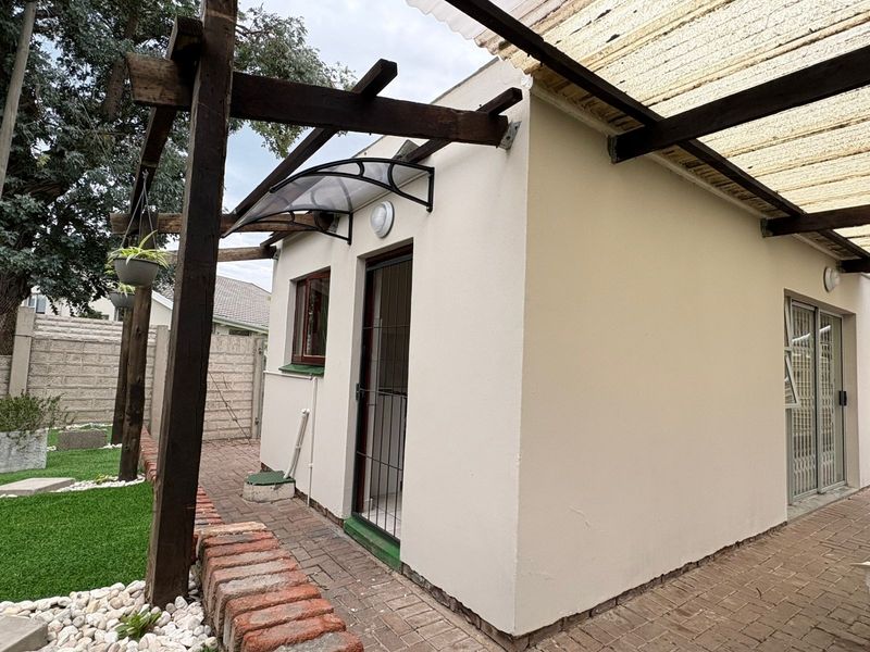 Rear exterior view of the cottage featuring a timber pergola, paved patio area, and secure access points with sliding doors.