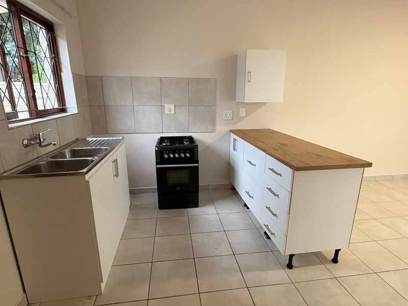 A clean, functional kitchen featuring white cabinetry, a wood-look countertop, a freestanding stove, and a double sink with tiled splashbacks.