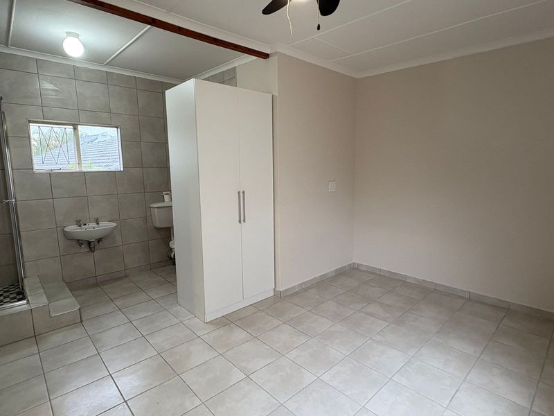 A clean, tiled bathroom featuring a shower enclosure, wall-mounted basin, and toilet, with a neutral color palette and functional layout.