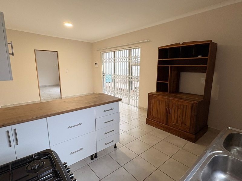 A functional kitchen featuring a central island with wooden countertop, white cabinetry, tiled flooring, and direct access to the patio through a security gate.