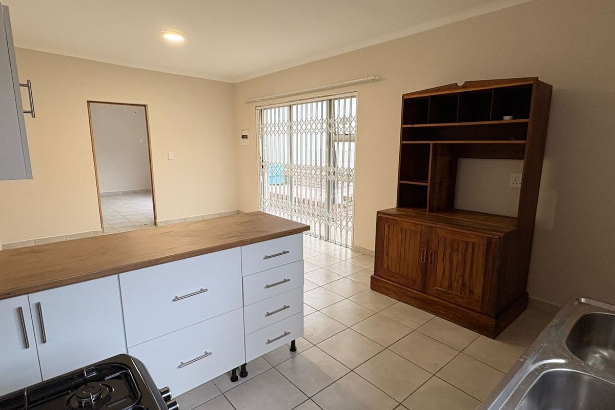 A functional kitchen featuring a central island with wooden countertop, white cabinetry, tiled flooring, and direct access to the patio through a security gate.