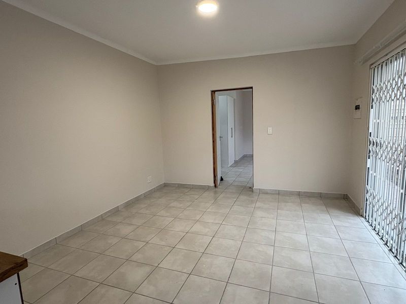 An empty, neutrally painted living area featuring tiled flooring and a secure metal sliding gate leading to the exterior.