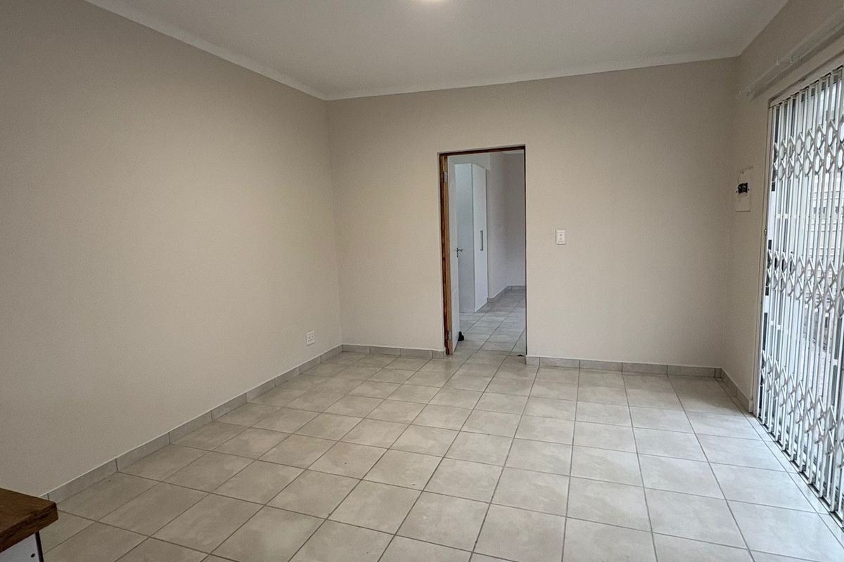 An empty, neutrally painted living area featuring tiled flooring and a secure metal sliding gate leading to the exterior.
