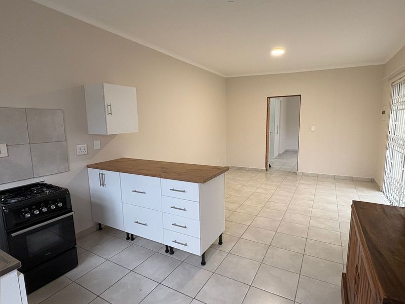 Open-plan living and kitchen area featuring tiled floors, modern white cabinetry with wooden countertops, and a freestanding gas stove.