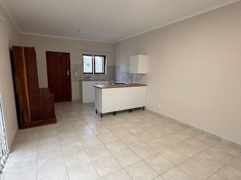 Open plan kitchen and living area featuring tiled flooring, neutral walls, and a functional kitchen island with a built-in hob.