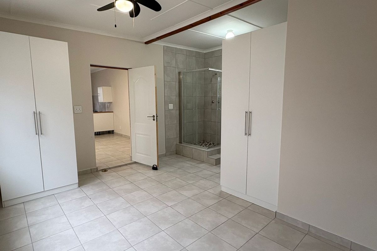 Spacious bedroom featuring neutral tiled flooring, built-in cupboards, a ceiling fan, and an en-suite shower room.