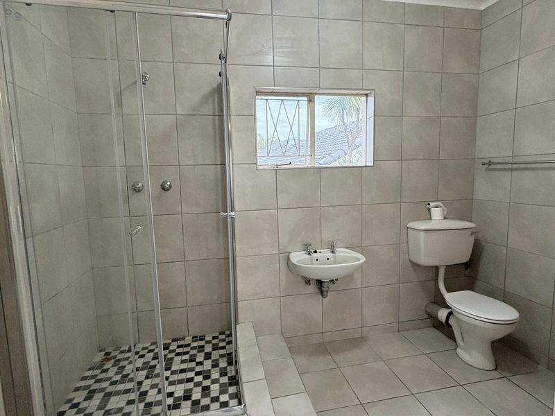 A functional bathroom featuring a glass shower enclosure, wall-mounted basin, and toilet, finished with neutral wall and floor tiling.
