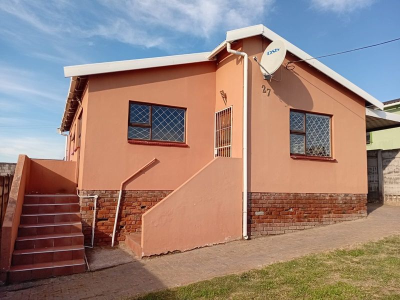 Front elevation of a single-story house featuring a brick base, tiled entrance stairs, security window bars, and a satellite dish installation.