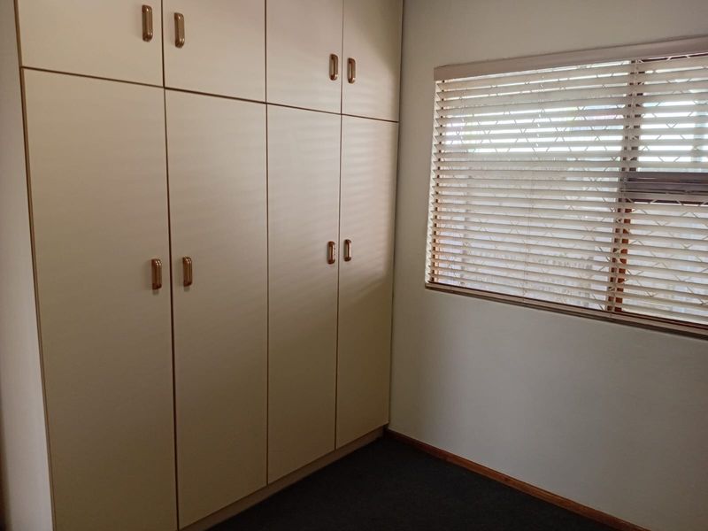 A clean, empty bedroom featuring floor-to-ceiling built-in cupboards and window blinds, offering a neutral space ready for personalization.