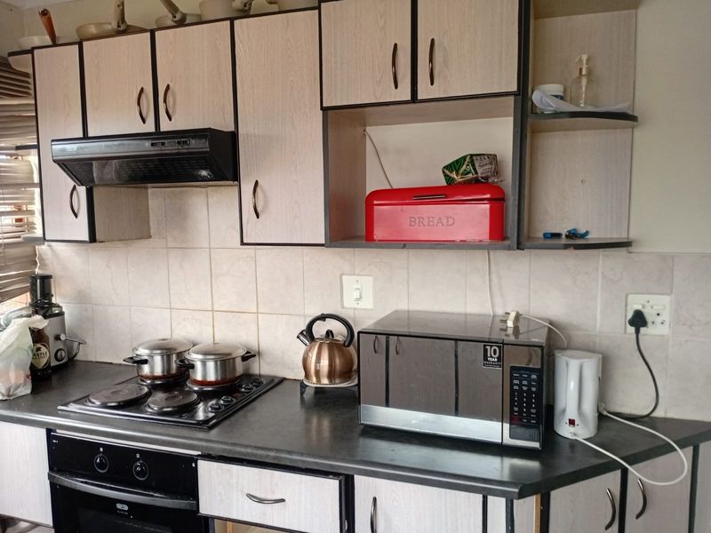 A functional kitchen featuring laminate cabinetry, a built-in oven, electric hob, extractor fan, and tiled splashback with a dark laminate countertop.