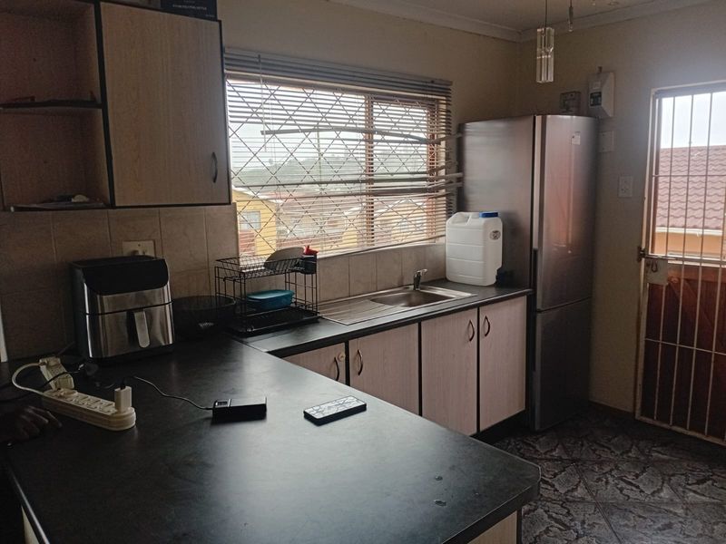 A functional kitchen featuring laminate cabinetry, dark countertops, a stainless steel sink, and tiled flooring with access to an exterior security gate.