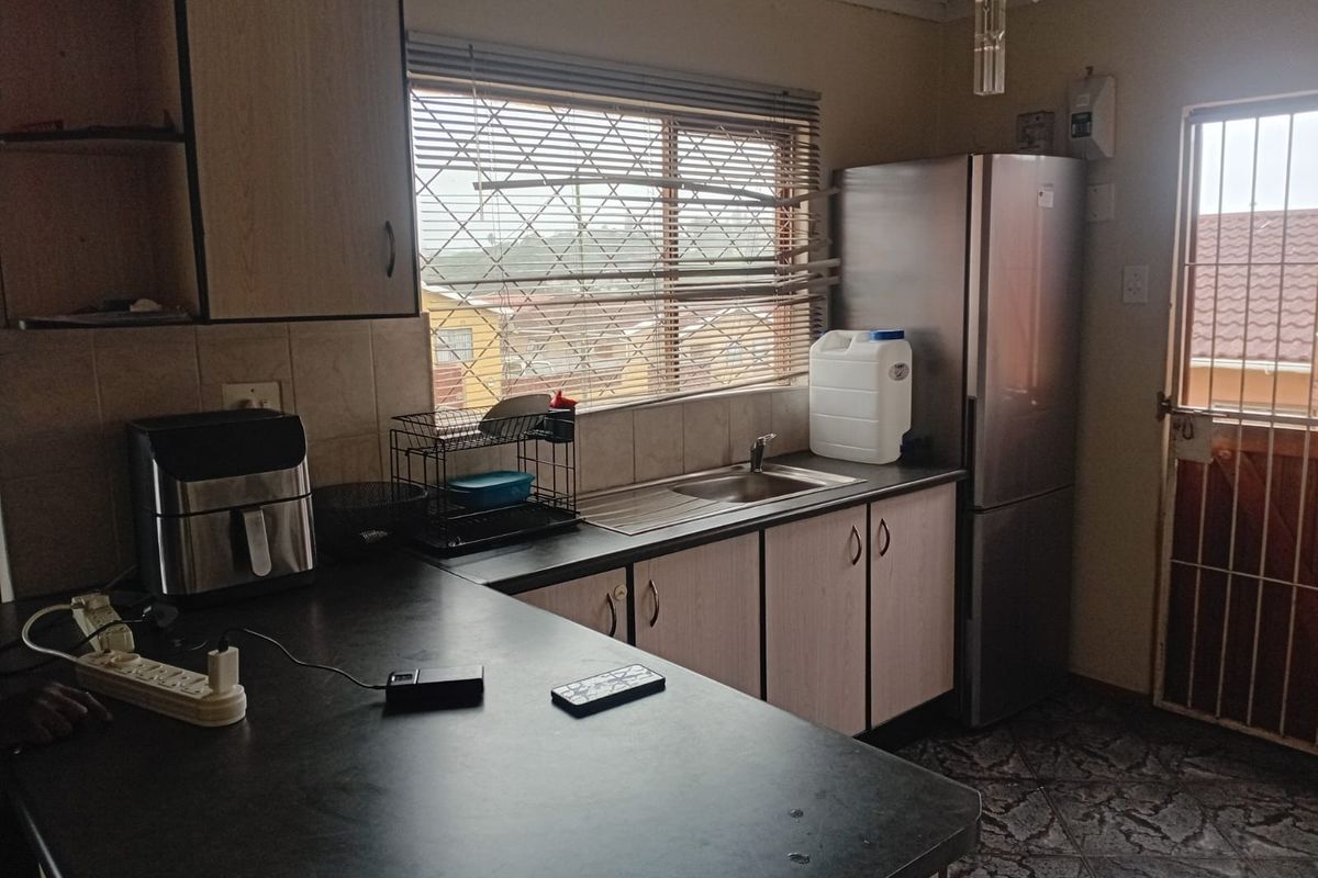 A functional kitchen featuring laminate cabinetry, dark countertops, a stainless steel sink, and tiled flooring with access to an exterior security gate.