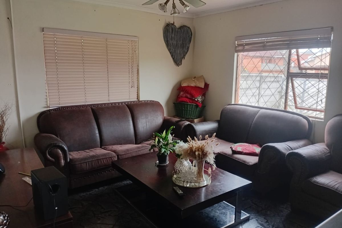 A comfortable living room featuring tiled flooring, a ceiling fan, and natural light provided by large windows with fitted venetian blinds.