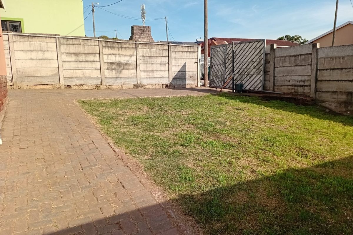 A rear yard featuring a paved area, a small lawn, and a precast concrete boundary wall with a metal sliding gate.
