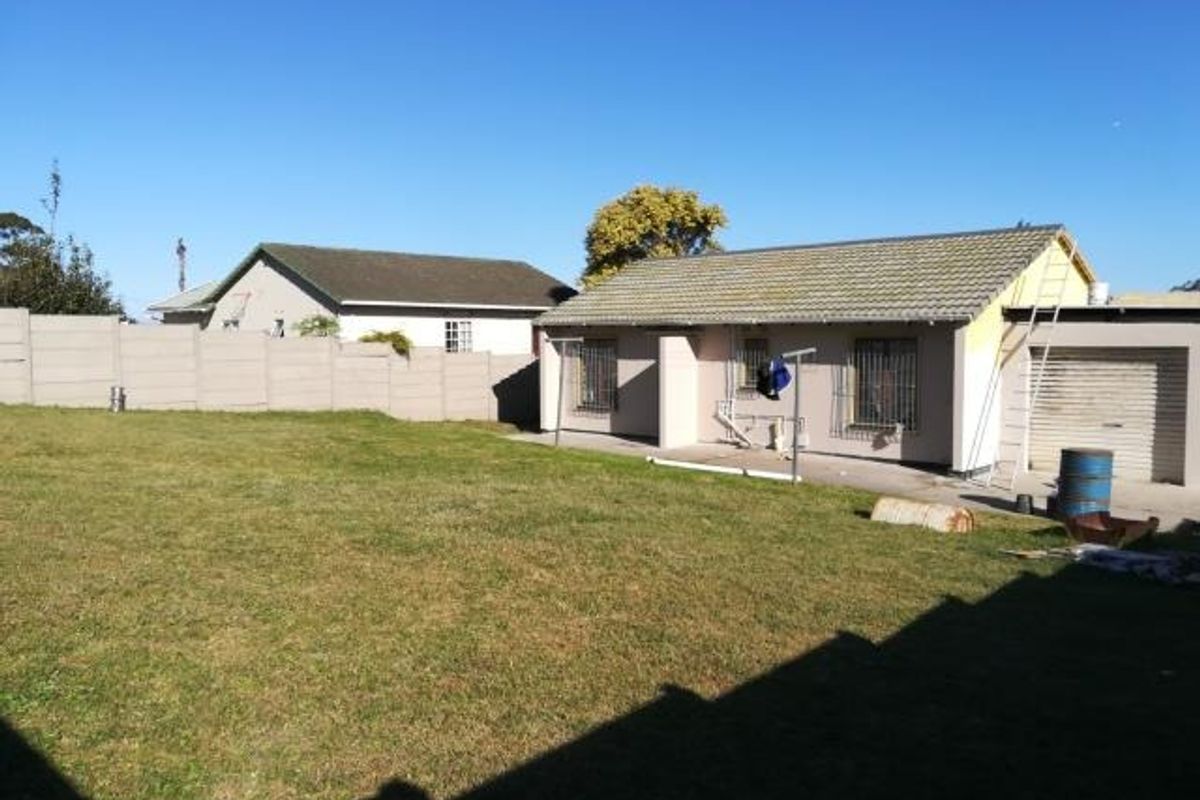 Rear view of the property featuring a large lawn, precast boundary wall, and a single garage with a tiled roof.