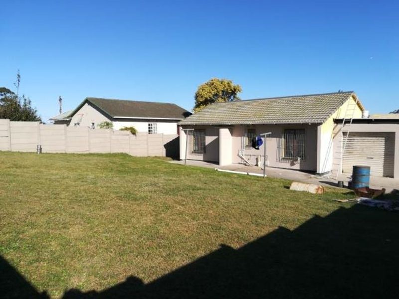 Rear view of the property featuring a large lawn, precast boundary wall, and a single garage with a tiled roof.