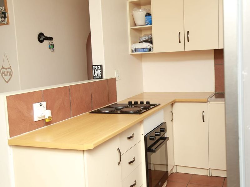 A functional kitchen featuring built-in cabinetry, laminate countertops, an electric hob, and an integrated oven with tiled backsplash and flooring.