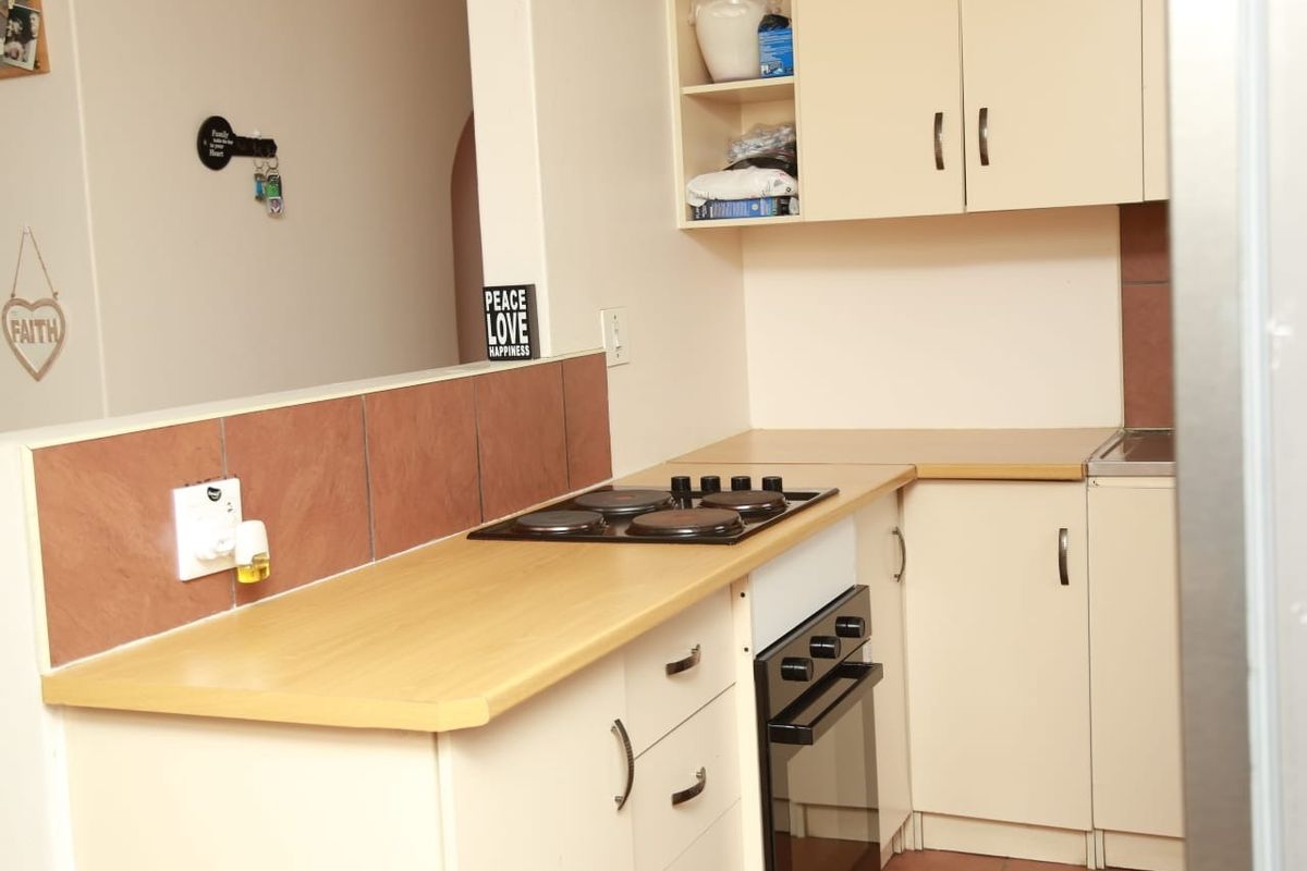 A functional kitchen featuring built-in cabinetry, laminate countertops, an electric hob, and an integrated oven with tiled backsplash and flooring.