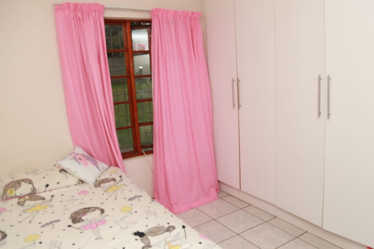 A bedroom featuring built-in cupboards, tiled flooring, and a wooden window frame, providing a functional and practical living space.