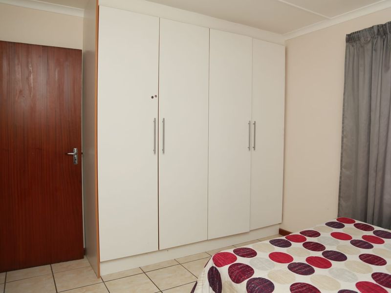 A bedroom featuring neutral tiled flooring and white built-in cupboards with modern handles, providing ample storage space.