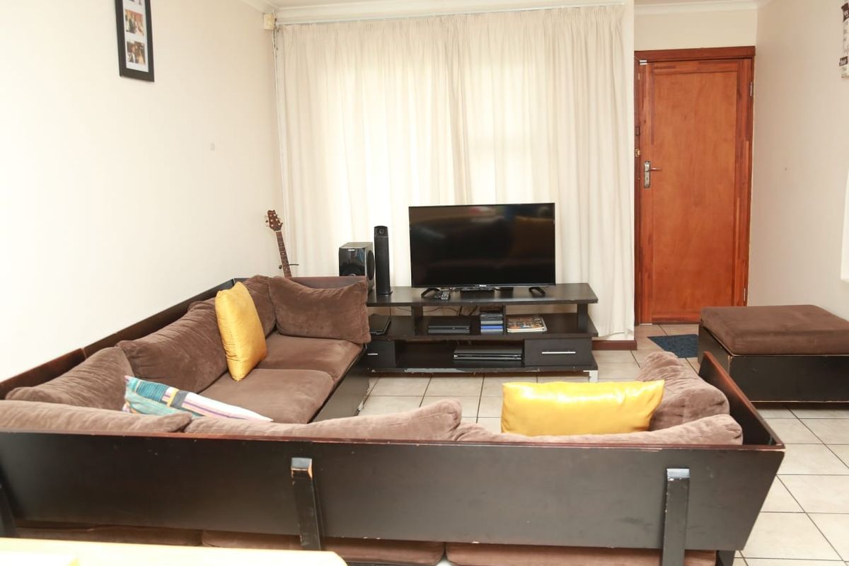 A functional living room featuring tiled flooring and a wooden entrance door, providing a neutral base for potential interior updates.