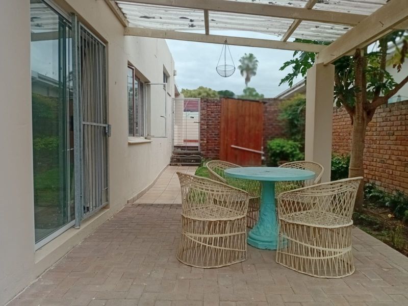 A covered patio area featuring brick paving, a sliding glass door with security gate, and access to a private rear garden space.