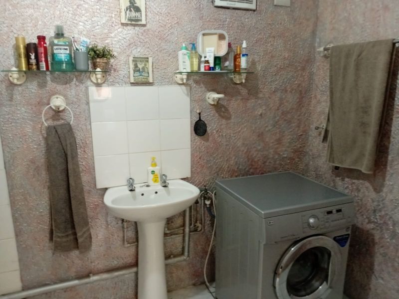 A functional laundry area featuring a pedestal basin, tiled splashback, and dedicated plumbing connections for a washing machine.