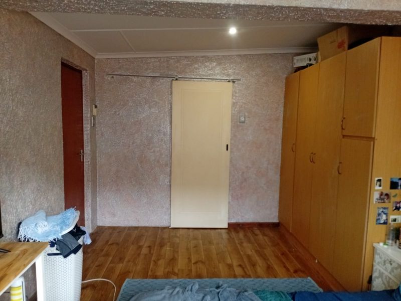 Bedroom featuring laminate flooring, built-in wooden cupboards, and a sliding door, with textured wall finishes throughout.
