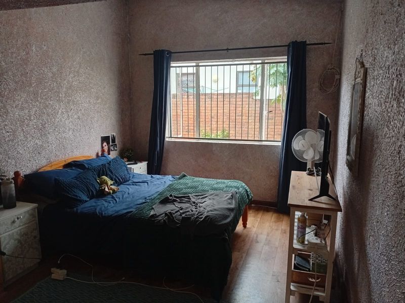 A bedroom featuring laminate flooring, textured walls, and a window fitted with security bars.