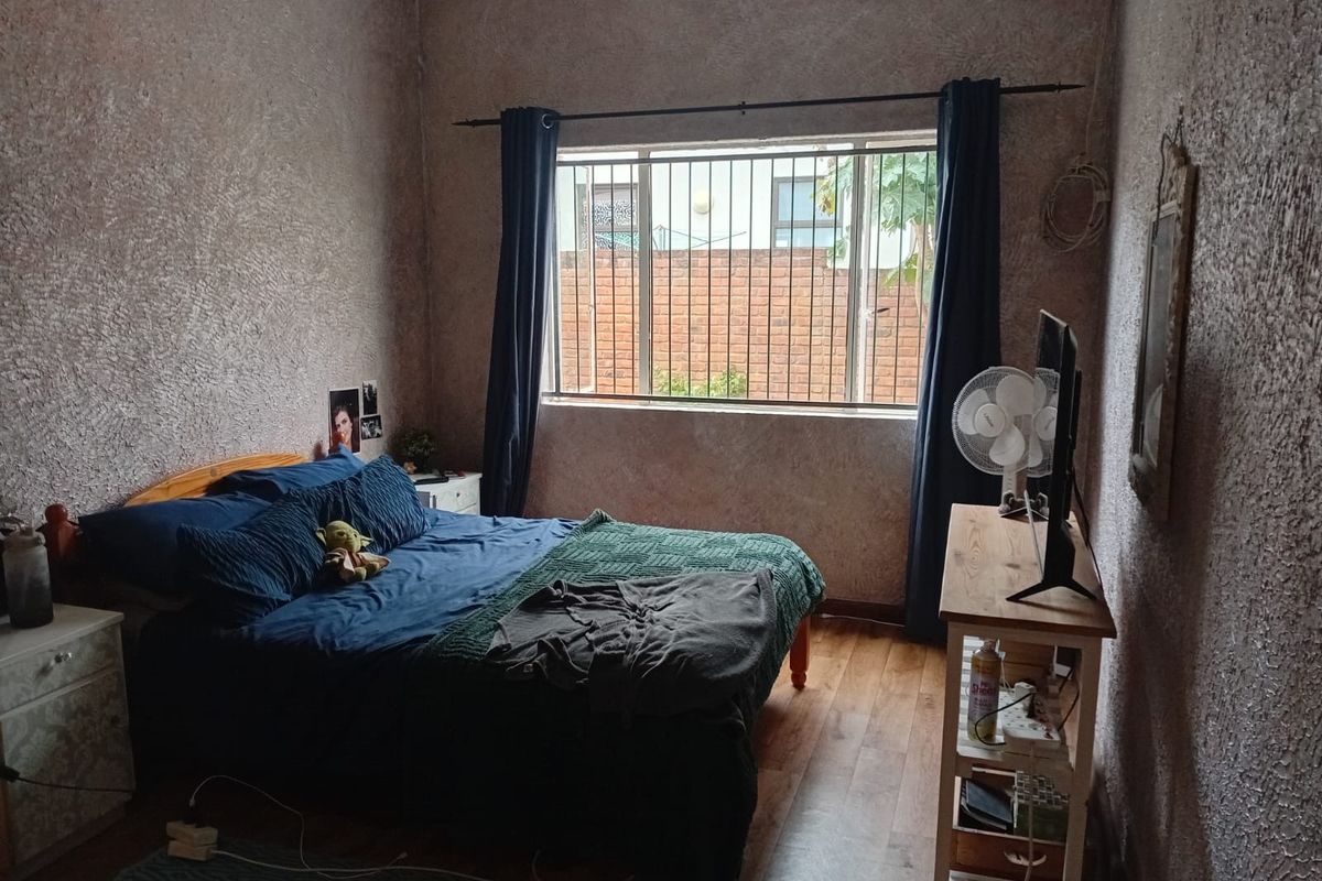 A bedroom featuring laminate flooring, textured walls, and a window fitted with security bars.