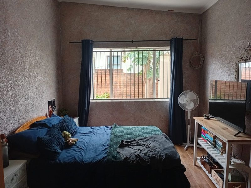 A bedroom featuring textured walls, laminate flooring, and a window fitted with security bars.