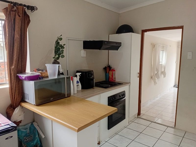 A functional kitchen featuring built-in cabinetry, an oven, hob, extractor fan, and tiled flooring, with a view leading into an adjacent hallway.