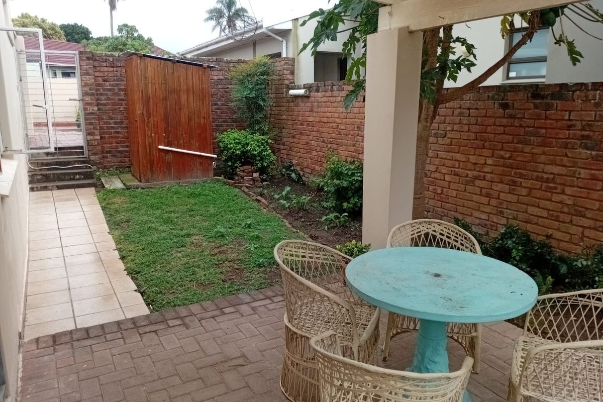 A private rear courtyard featuring a paved patio area, a pergola, a small lawn, and a brick boundary wall.