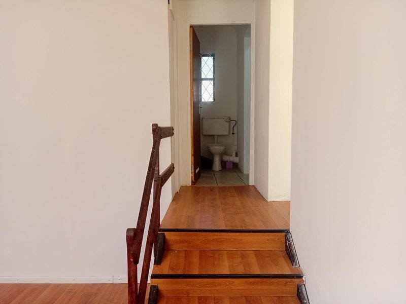A view of a hallway featuring a wooden staircase leading towards a bathroom with a visible toilet and window.