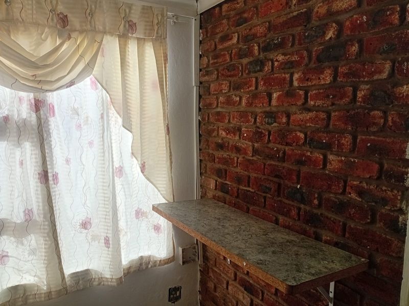 A small interior space featuring an exposed brick wall, a built-in shelf, and a window with curtains.