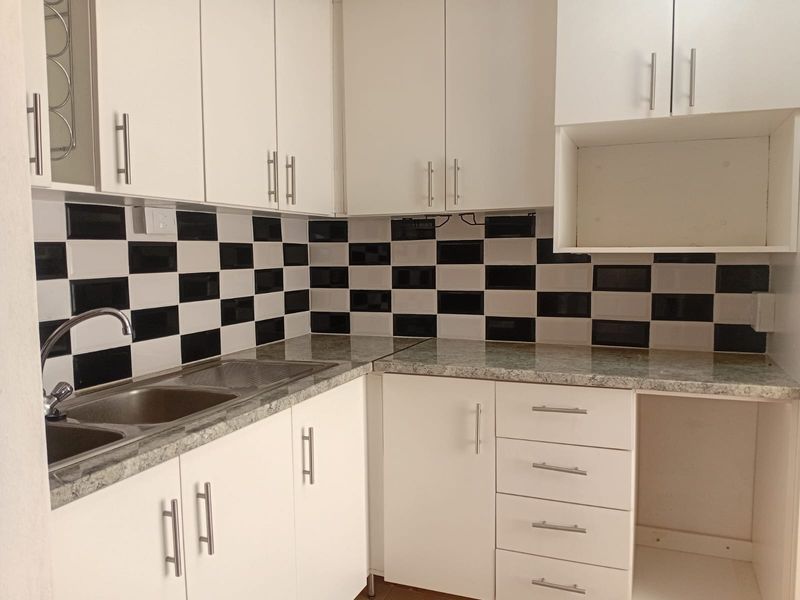 A clean, functional kitchen featuring white cabinetry, granite-look laminate countertops, and a distinctive black and white checkered tile backsplash.