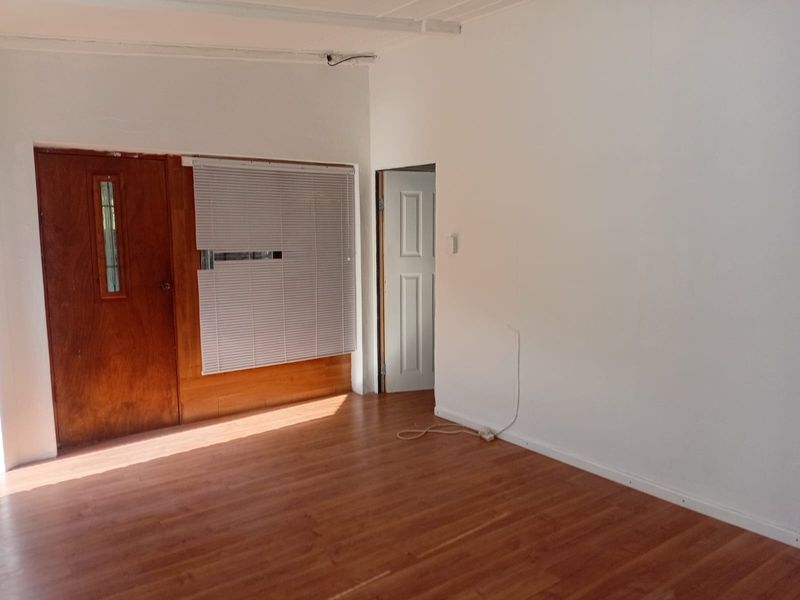 An empty living room featuring laminate flooring, timber door, and venetian blinds, requiring minor cosmetic attention to wall finishes and exposed wiring.