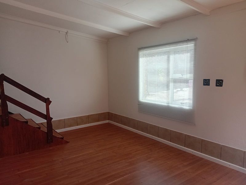 An empty living area featuring laminate flooring, exposed ceiling beams, a wooden staircase, and tiled skirting, with some electrical fixtures requiring completion.