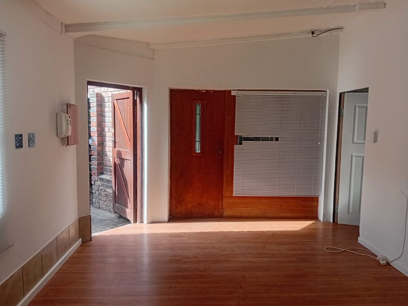 An empty living area featuring laminate flooring, timber doors, and venetian blinds, offering a blank canvas for potential interior updates.