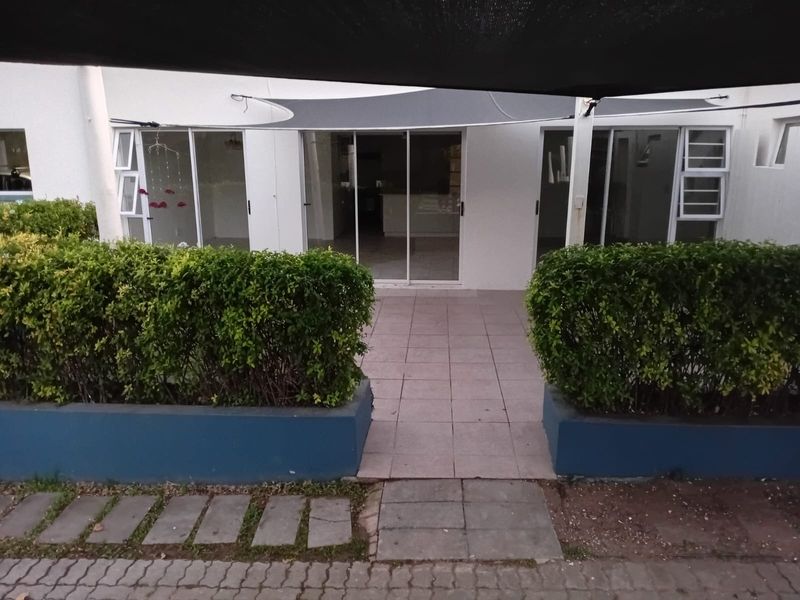 Rear exterior view of the flat featuring a paved patio area, raised garden beds, and sliding glass door access to the interior living space.