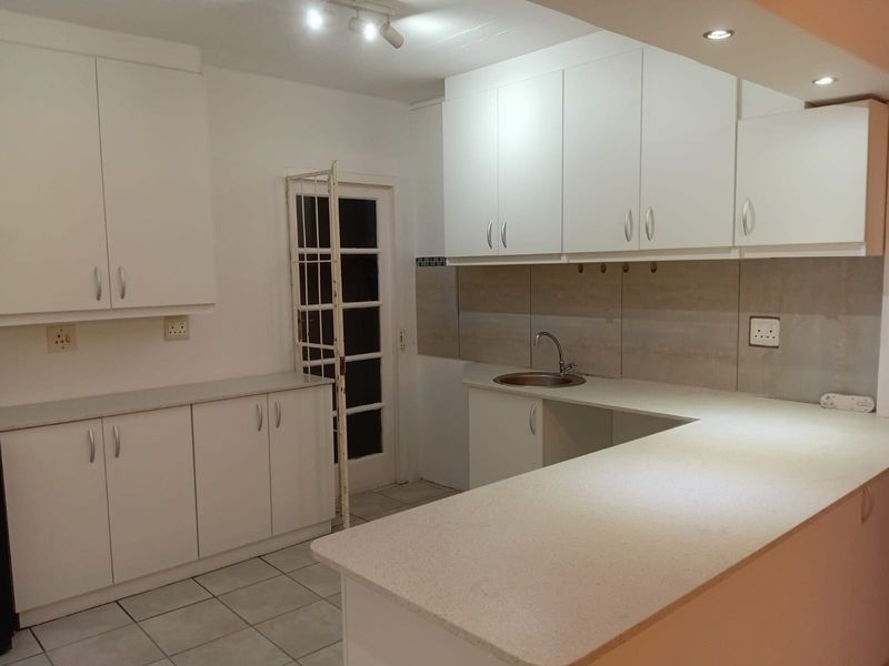 A clean, functional kitchen featuring white cabinetry, stone countertops, a tiled backsplash, and neutral floor tiles, offering a bright and practical workspace.