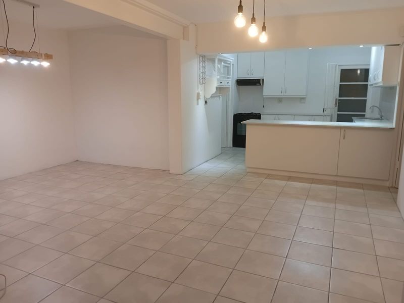 Spacious open-plan living and kitchen area featuring neutral tiled flooring, white cabinetry, a functional peninsula, and modern pendant lighting.