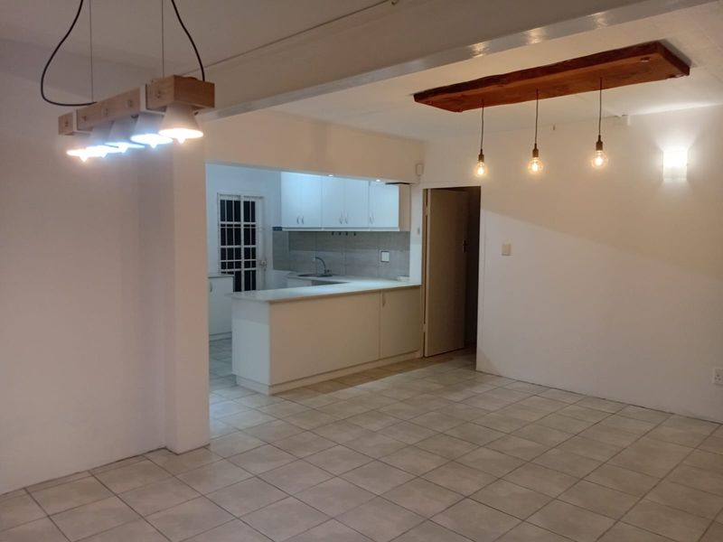 An open-plan living and kitchen area featuring tiled flooring, modern pendant lighting, and a functional kitchen with white cabinetry and a breakfast counter.