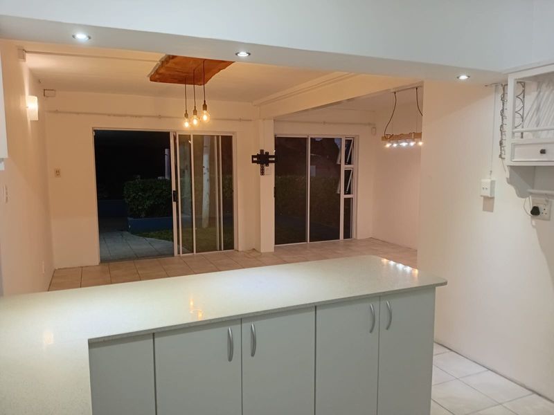 Spacious open-plan living area featuring a modern kitchen island with stone countertops, tiled flooring, and large sliding glass doors leading to the exterior.