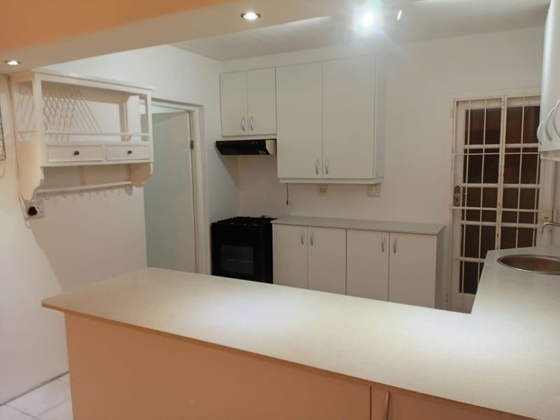 A functional kitchen featuring white built-in cabinetry, laminate countertops, a stainless steel sink, and a freestanding stove with an extractor fan.