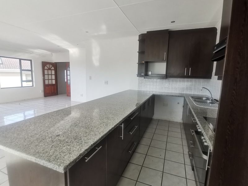 Open-plan kitchen featuring dark wood cabinetry, granite countertops, and integrated appliances, flowing into a spacious, tiled living area.