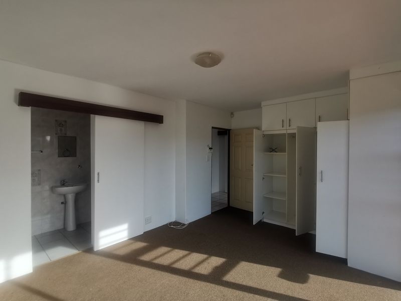 Spacious bedroom featuring built-in cupboards and an en-suite bathroom with a pedestal basin.