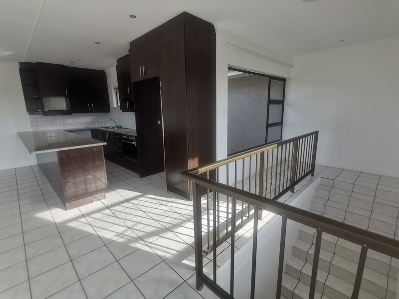 Open-plan kitchen featuring dark wood cabinetry, granite countertops, and tiled flooring, adjacent to a staircase with a metal balustrade.