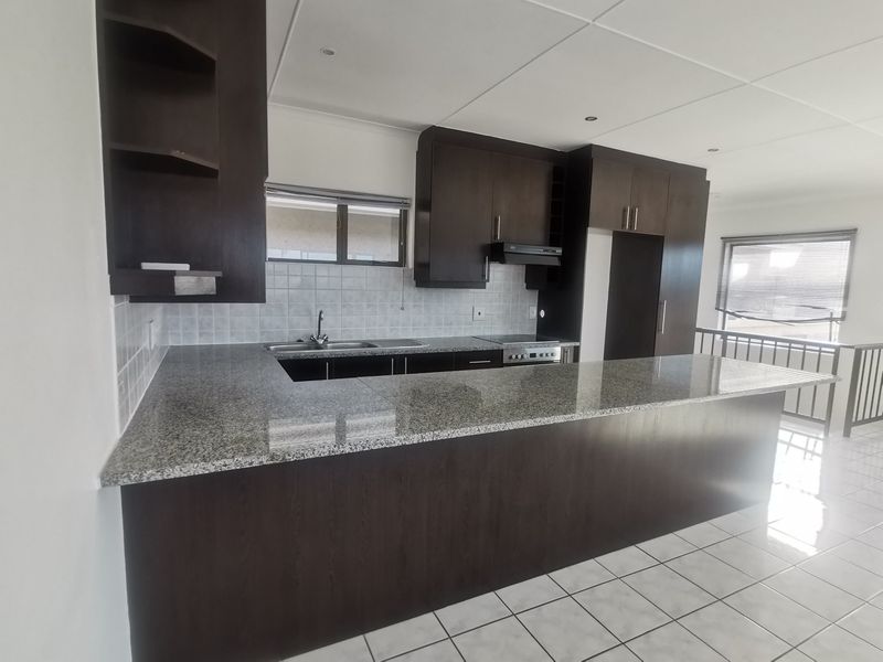 A spacious, modern kitchen featuring dark wood cabinetry, granite countertops, a breakfast bar, and tiled flooring in an open-plan layout.